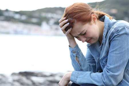 Sad casual woman complaining alone crying on the beach  with bad weatherの写真素材