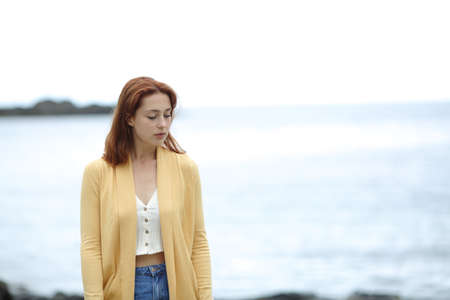 Front view of a sad pensive woman walking alone on the beach
