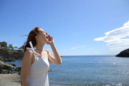 Happy woman in white dress screaming on the beach on summer vacation