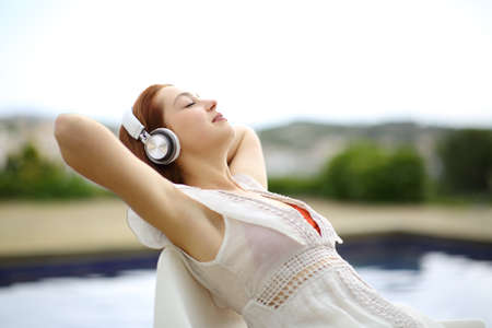 Relaxed woman wearing headphones listening to music resting in a poolの写真素材