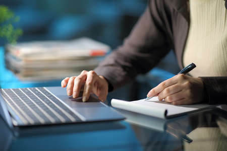 Close up of a woman hands taking notes using laptop in the night at home or office