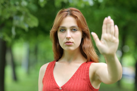 Serious redhead woman gesturing stop with her hand standing in a parkの写真素材