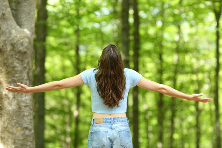 Back view of a happy woman outstretching arms in a forest
