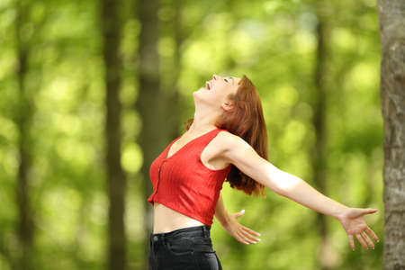 Profile of an excited woman stretching arms screaming loud in a forest