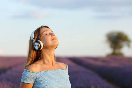 Relaxed woman meditating listening music and breathing in lavender field at sunset