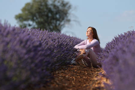 Relaxed woman resting sitting in a lavender field with closed eyesの写真素材
