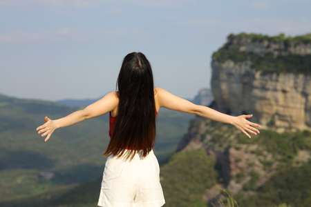 Back view portrait of a woman outstretching arms contemplating in the mountain