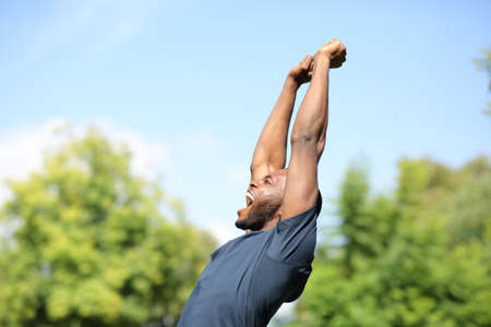 Side view portrait of an excited black man raising arms in a parkの写真素材