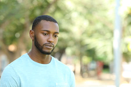 Sad black man looking away distracted walking in a park