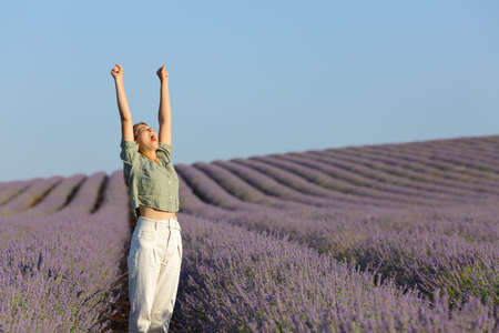 Casual woman raising arms in lavender field celebrating vacationの写真素材