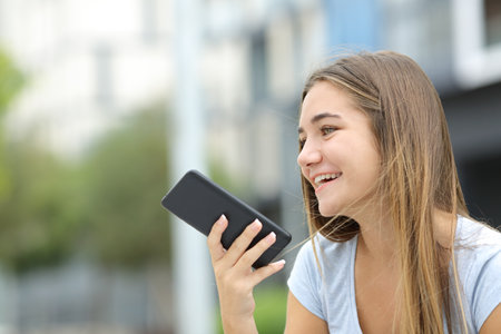 Happy teen using voice recognition on smart phone in the streetの写真素材