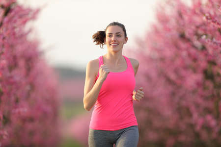 Front view of happy runner running towards camera in a pink flowered fieldの写真素材