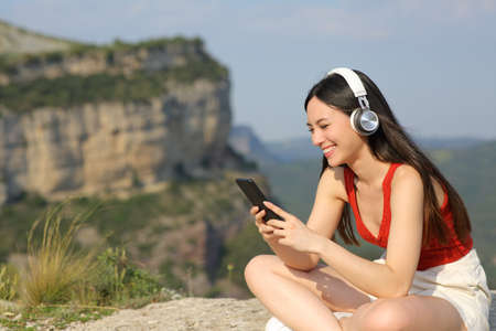 Happy asian woman wearing headphones listening to music in a cliffの写真素材