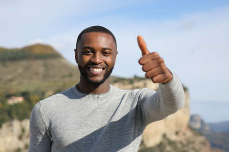Happy man with black skin gesturing thumb up in the mountainの写真素材
