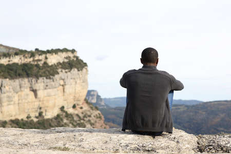 Back view portrait of a man with black skin sitting in nature contemplating viewsの写真素材