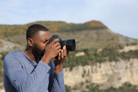 Side view portrait of a man with black skin taking photos with dslr camera in the mountainの写真素材