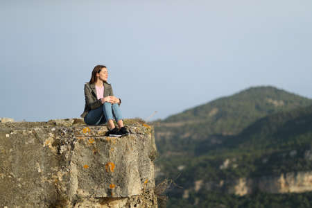 Casual woman sitting contemplating views from the top of a cliff in the mountainの写真素材