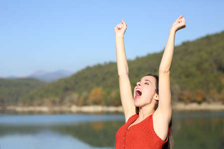 Euphoric woman celebrating vacation raising arms in summer in a lakeの写真素材