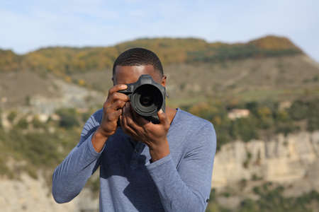 Front view portrait of a man with black skin taking photos with dslr camera in natureの写真素材