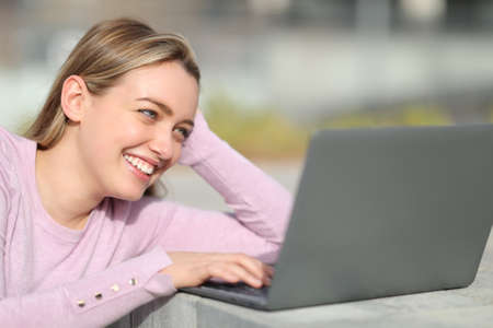 Happy teen using laptop to watch media content sitting in the streetの写真素材