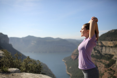 Side view portrait of a sportswoman stretching arms in a beautiful landscapeの写真素材
