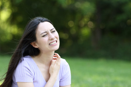Stressed asian woman scratching neck sitting in a green parkの写真素材