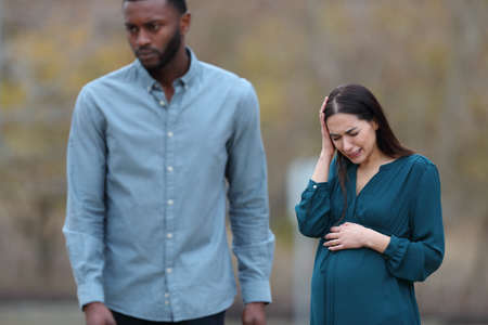 Front view portrait of a breakup with a husband leaving his sad pregnant wife in a parkの写真素材