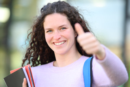 Happy student with thumbs up looking at camera in a campusの写真素材