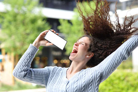 Happy woman singing in the street showing blank phone screenの写真素材