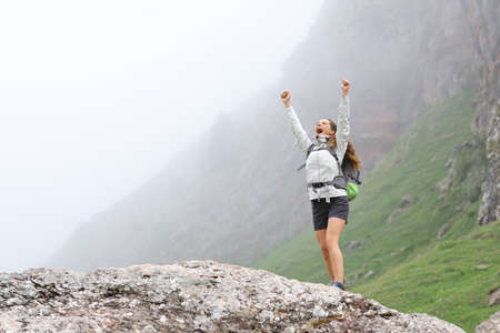 Excited trekker raising arms celebrating success in the mountain a foggy day