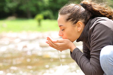 Side view portrait of a woman drinking water from river in the mountainの写真素材