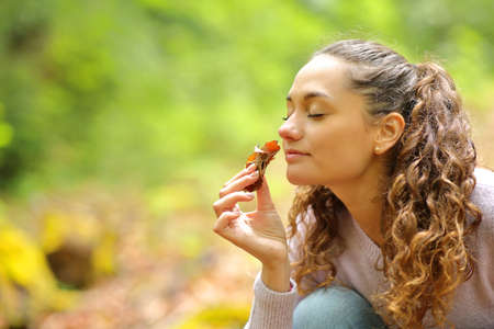 Happy woman smelling dead leafs in a forest