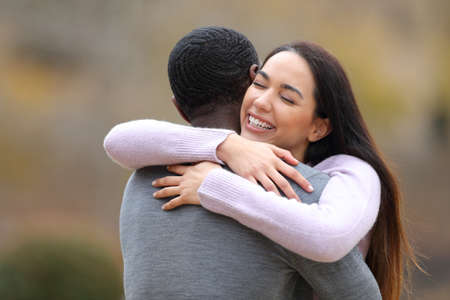 Happy woman meeting and hugging a man with black skin in a parkの写真素材