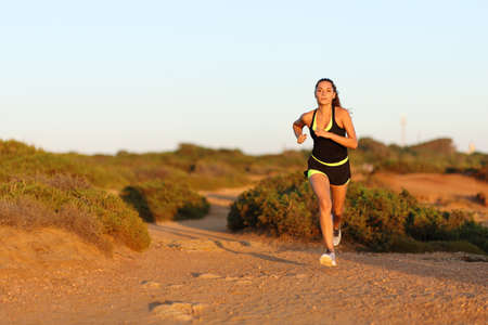 Runner woman running towards camera at sunset in the mountain