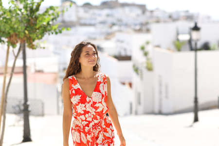 Happy woman in red walking in a white town street on summer vacationの写真素材