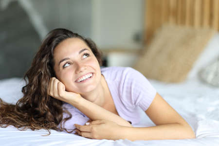Happy woman looking at side and above lying on the bedの写真素材