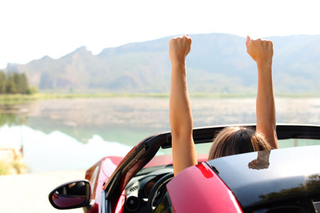 Back view portrait of a driver celebrating rsising arms in a convertible carの写真素材