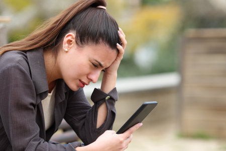 Worried teen complaining checking bad news on mobile phone in a parkの写真素材
