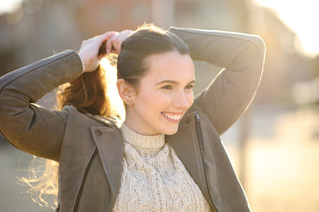 Happy woman making pony tail at sunset in the streetの写真素材