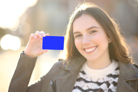 Happy woman showing credit card at camera in the street at sunsetの写真素材