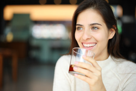 Happy woman drinking soda in a restaurant looking away in a restaurant