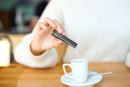 Close up portrait of a woman hand throwing suggar in a coffee cup in a bar