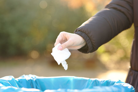Close up of a woman hand throwing trash into paper bin in winter in a parkの写真素材