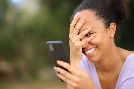 Embarrassed black woman using smart phone and looking at youの写真素材