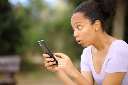 Amazed black woman checking phone content in a parkの写真素材