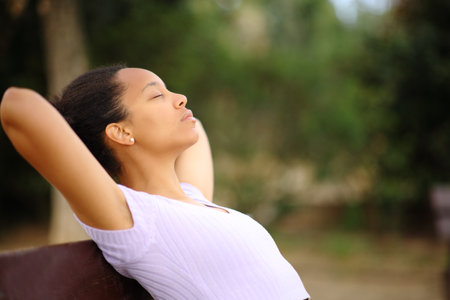 Profile of a relaxed black woman resting with hands on head sitting in a parkの写真素材