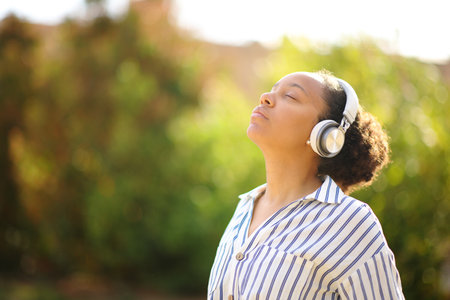 Black woman meditating using headphone in a park