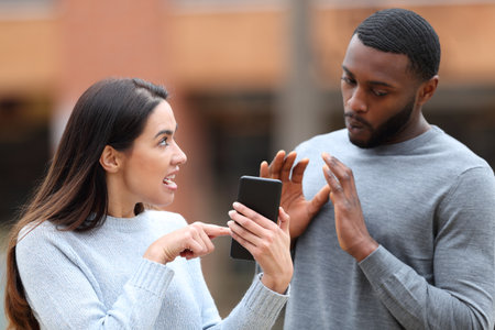 Angry woman scolding a shocked man showing cell phone content in the streetの写真素材