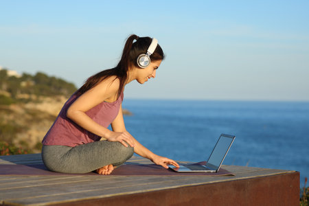 Yogi with headphone and laptop preparing online guided class on the beachの写真素材