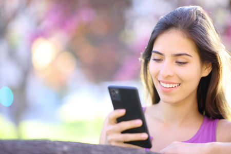 Happy woman using smart phone in a beautiful violet parkの写真素材